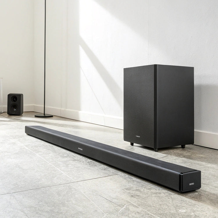 Barre de son noire allongée accompagnée d’un caisson de basses cubique noir, posées sur un sol clair devant un mur blanc épuré.